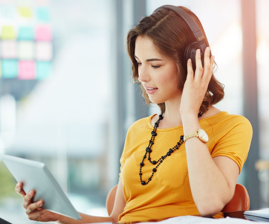 Woman wearing headphones appearing engaged in learning being viewed on a tablet.