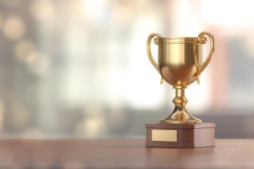 Golden trophy cup with walnut wooden base sitting on a desk