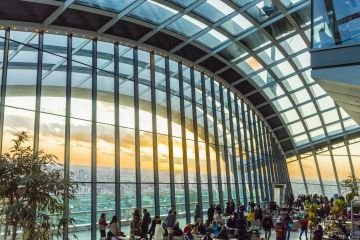 Sky Garden London: Indoor garden with large glass windows showing a city view at sunset, filled with people enjoying the space.