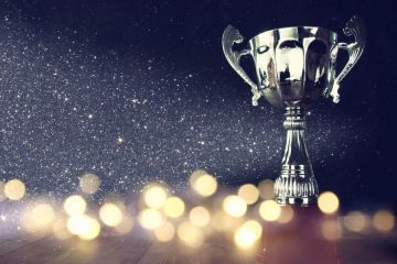 Silver trophy cup on wooden surface with sparkling lights and glittering background celebrating success.